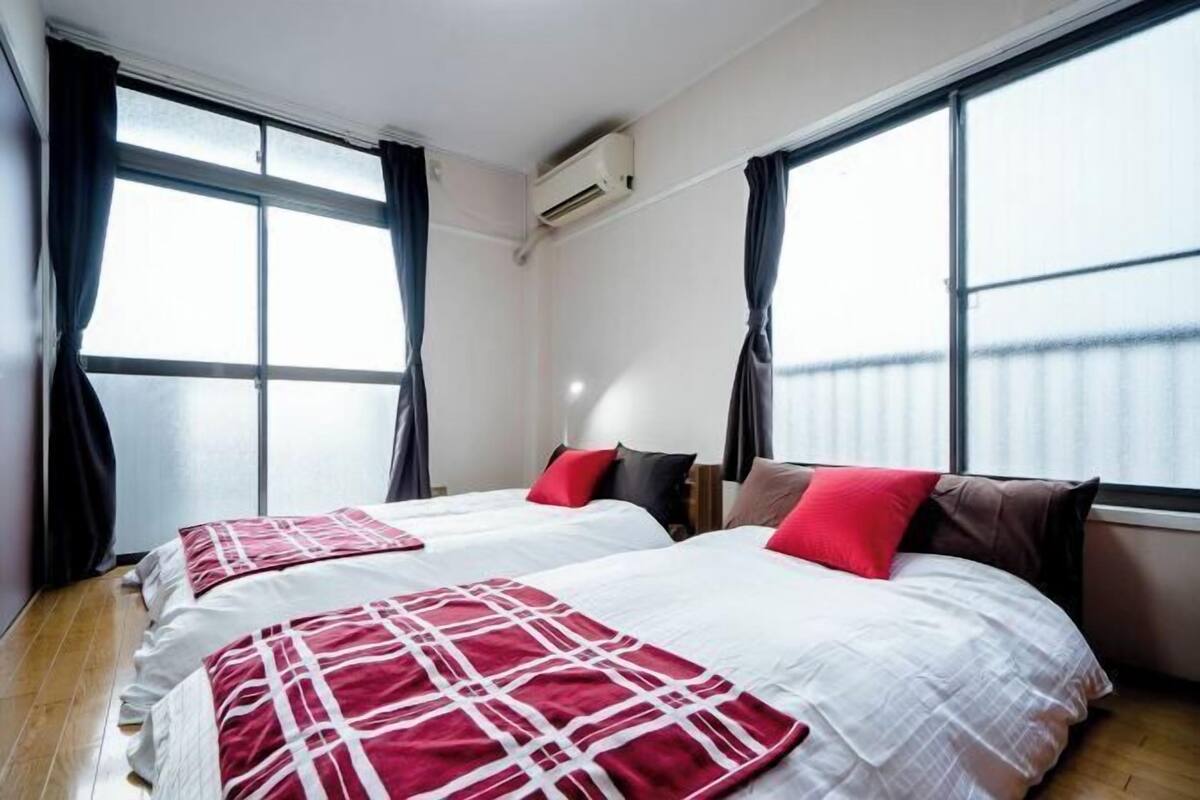 A hotel room with two beds, large windows, an air conditioning unit, and a wooden floor.