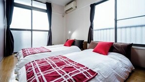 A hotel room with two beds, large windows, an air conditioning unit, and a wooden floor.