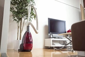Habitació amb un aspirador, una televisió sobre un suport i una planta en test.