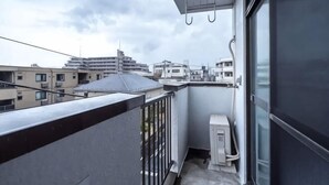 A balcony with a view of surrounding buildings, a window, and a small utility box.