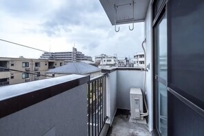 Un balcó amb vista a edificis als voltants, una finestra i una petita caixa de serveis.