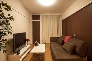 Ein gemütlicher Wohnraum mit Flachbildfernseher, kleinem Tisch, einer Couch, einer Pflanze und einem Schiebetürenschrank.
