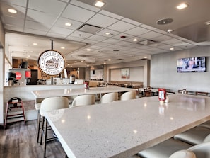 A spacious restaurant with a long counter, multiple seating areas, and a television screen on the wall. - Candlewood Suites Tacoma Mall by IHG (Tacoma)