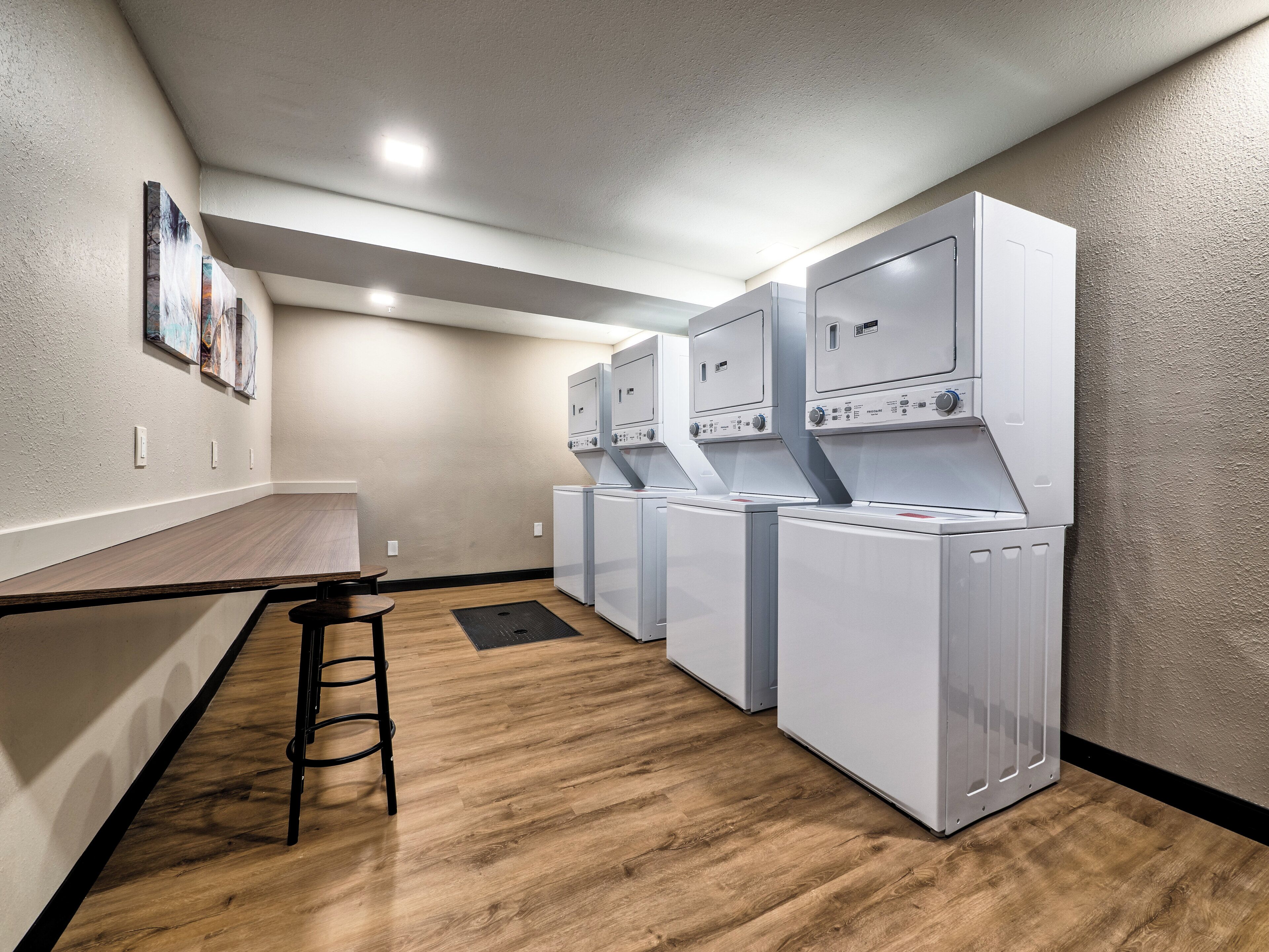 A laundry room with a wooden floor, a bar stool, and three stacked washing machines.