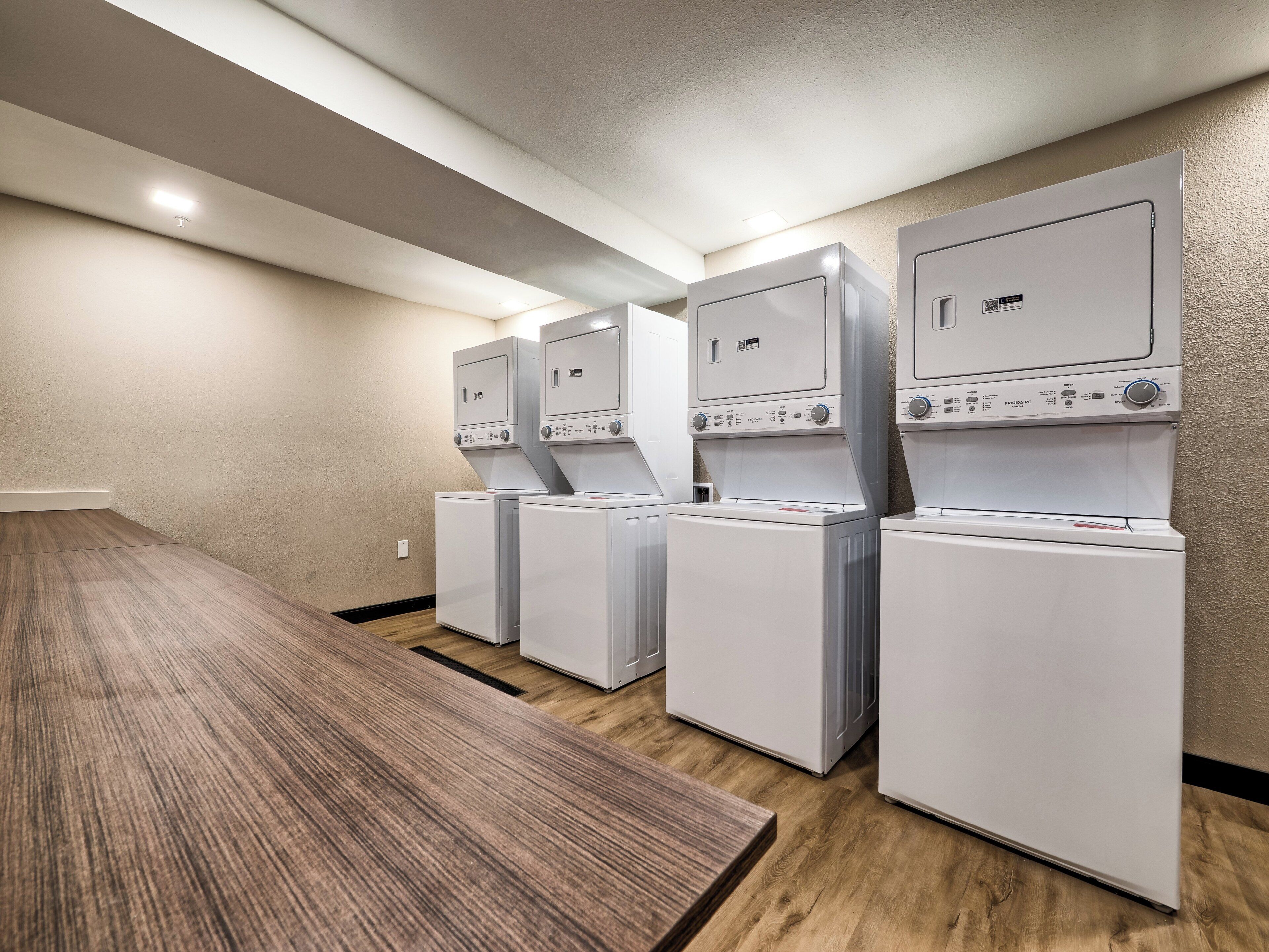 A laundry room with four stacked washers and dryers, a wooden table, and beige walls.