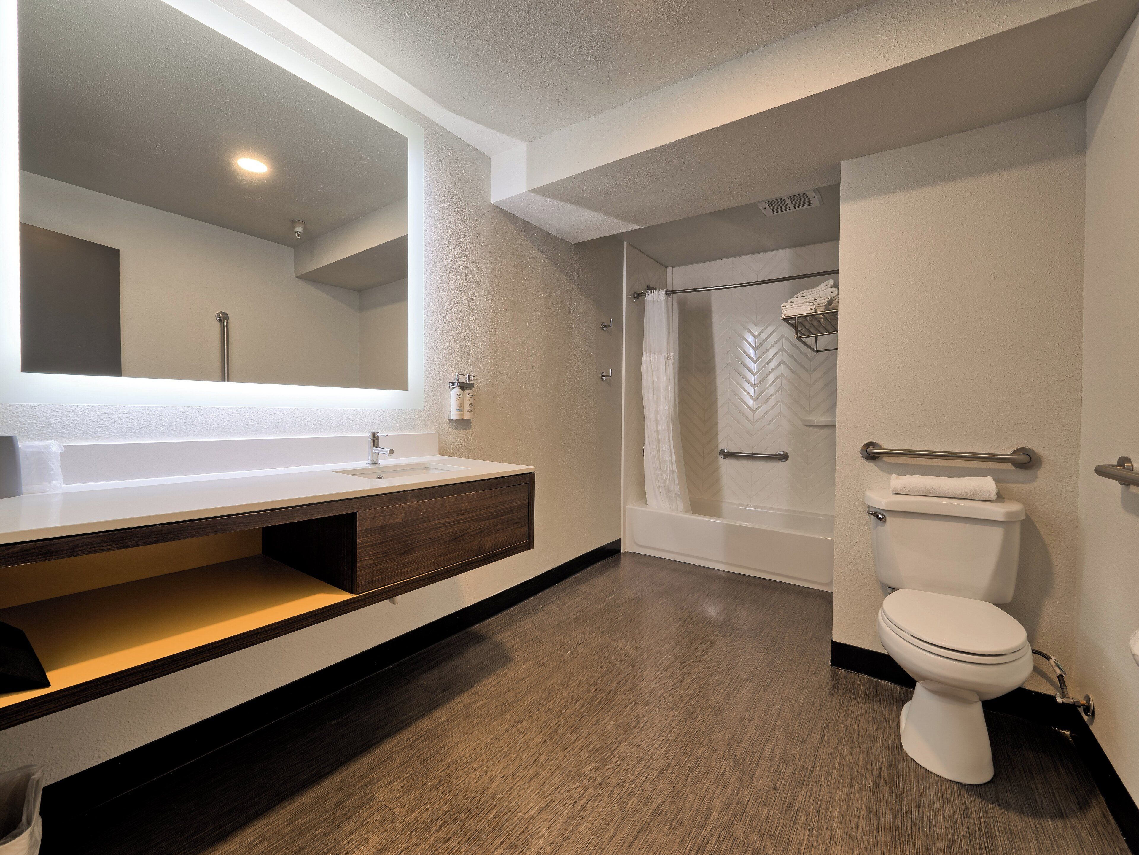 A modern bathroom with a large mirror, a white sink, a shower, and a toilet.