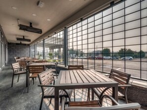 Ein modernes Café mit Holztischen und -stühlen, großen Fenstern und Blick auf einen Parkplatz.