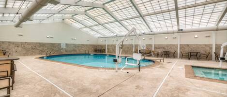 An indoor swimming pool with clear water, surrounded by beige tiles and equipped with a diving board and lounge chairs.
