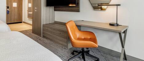 A hotel room with a bed, a desk with a chair, a flat-screen TV, a mirror, and a lamp.