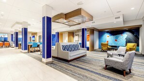 A hotel lobby with a sofa, armchairs, a map wall, and a seating area with tables.