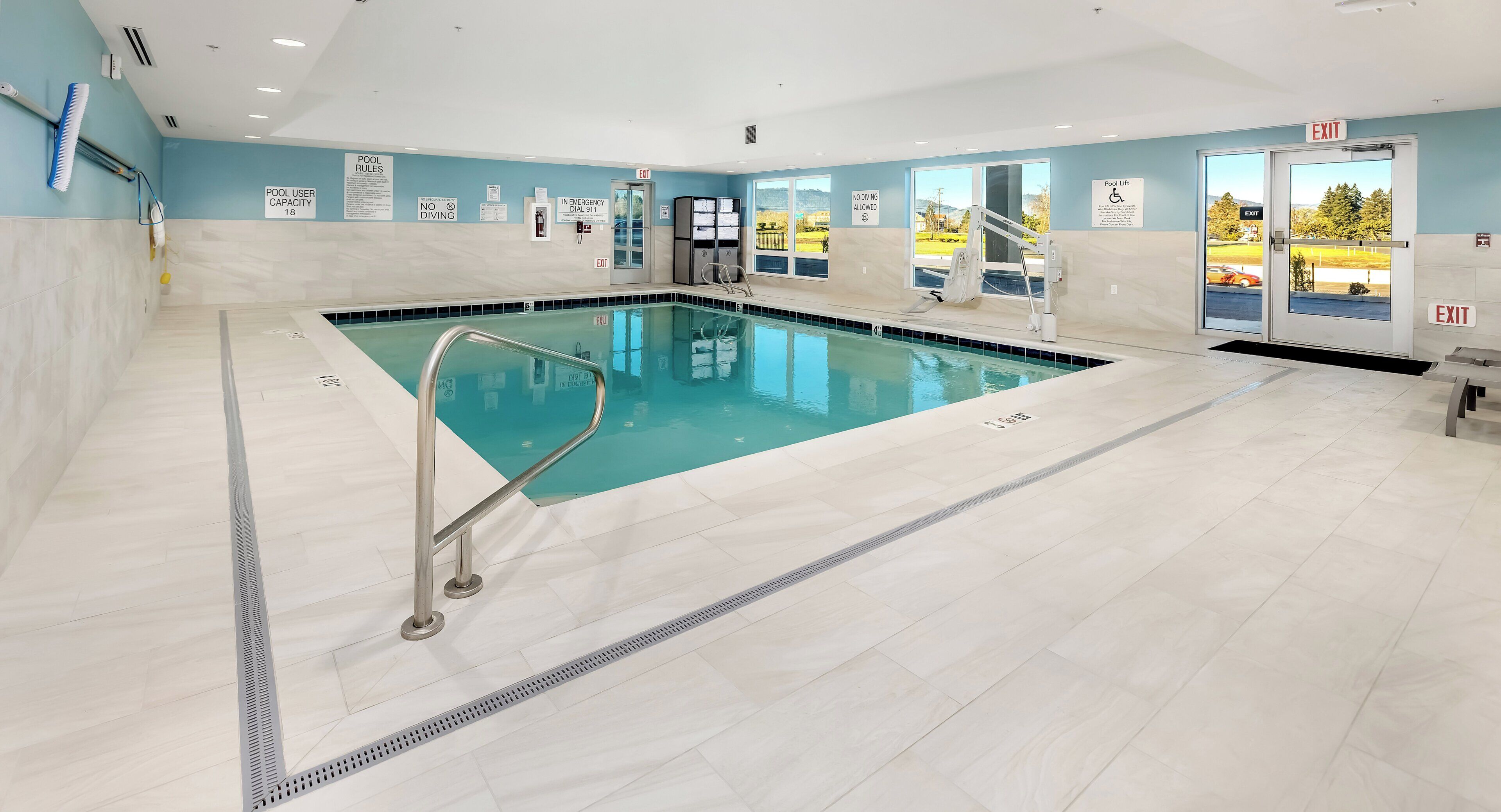 An indoor swimming pool with clear pool rules, a lifeguard chair, and an exit door.