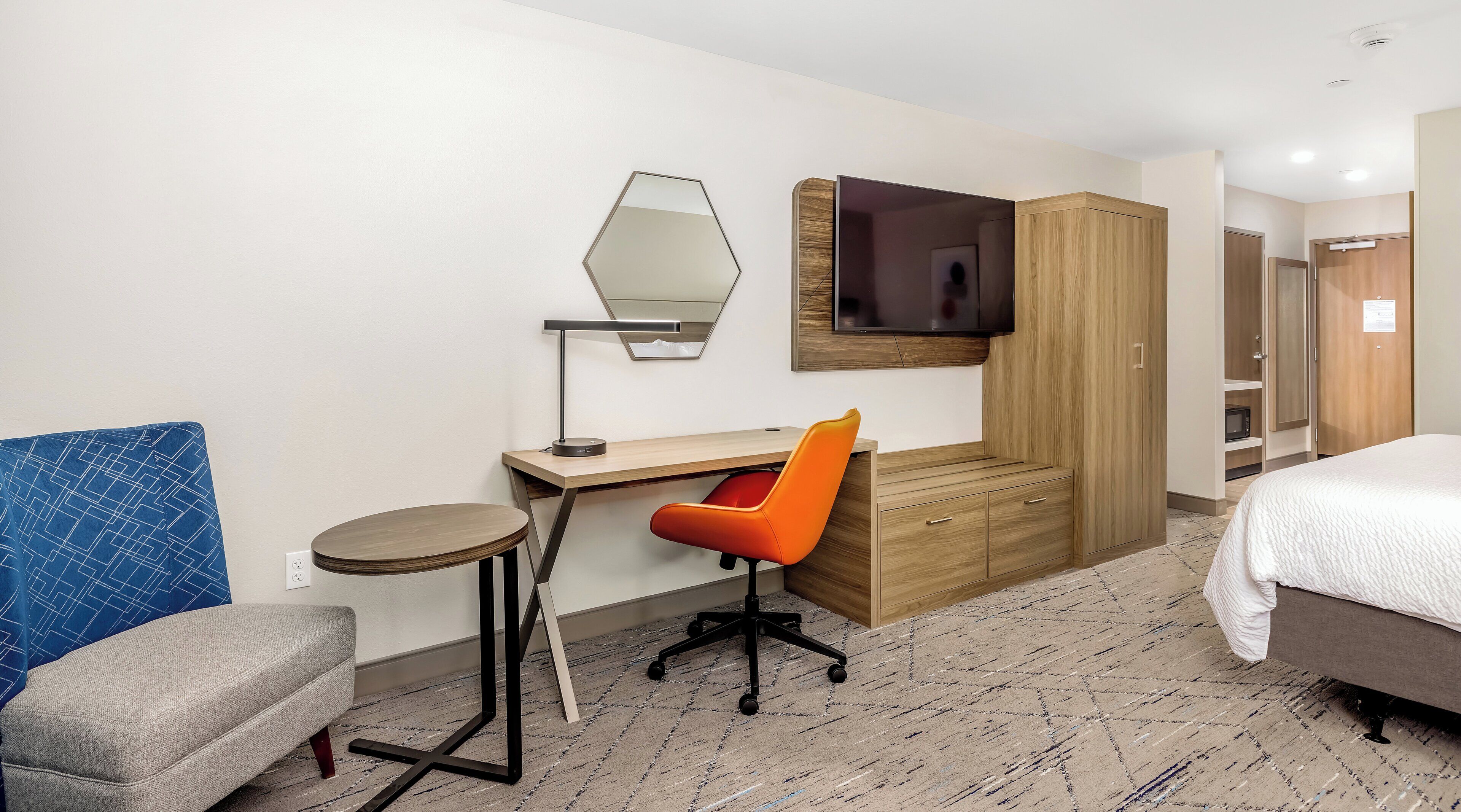A hotel room with a bed, a desk with a chair, a TV, a mirror, and a wardrobe.