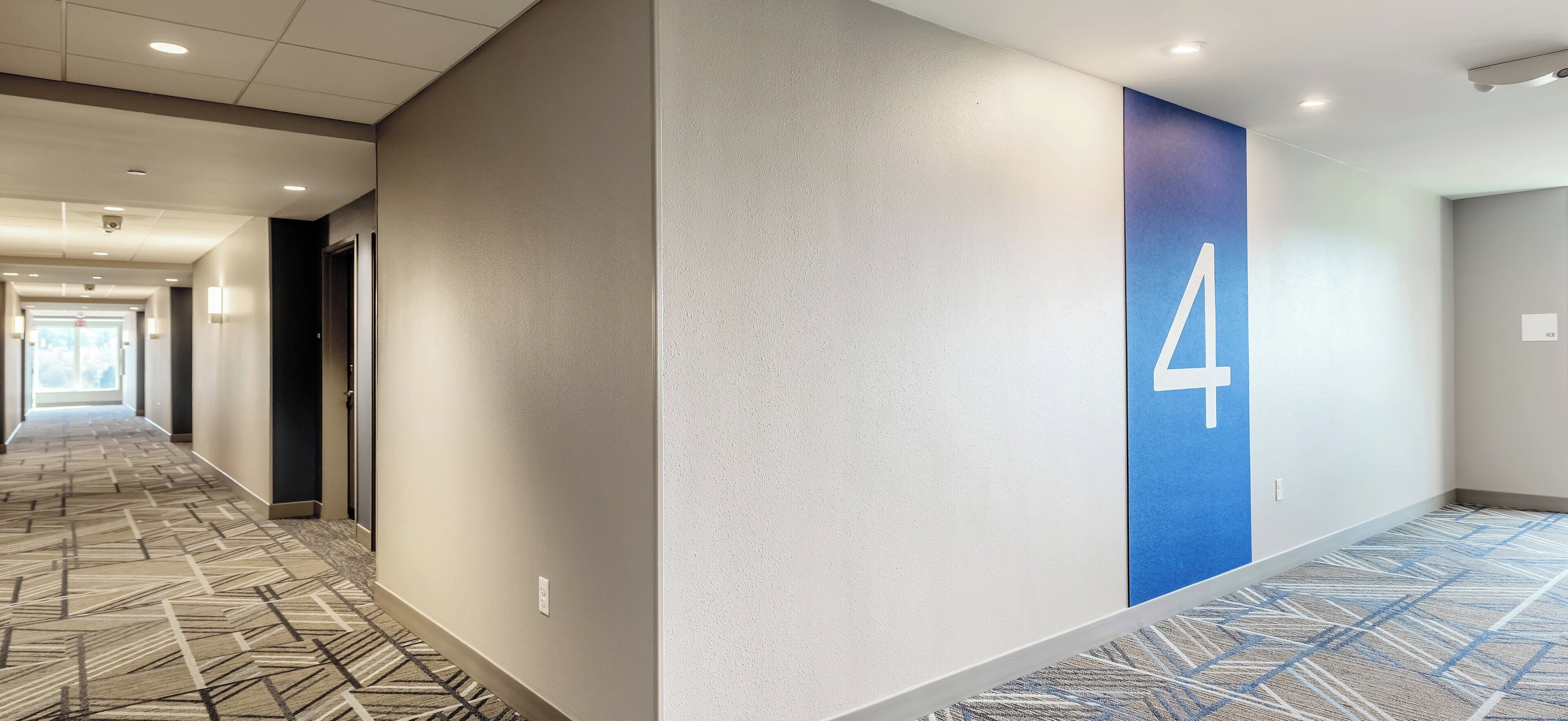 A hotel hallway with carpeted floors, a number 4 on the wall, and a door on the left.