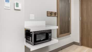 A kitchen with a microwave on a white shelf, a wooden door, and a wall-mounted thermostat.