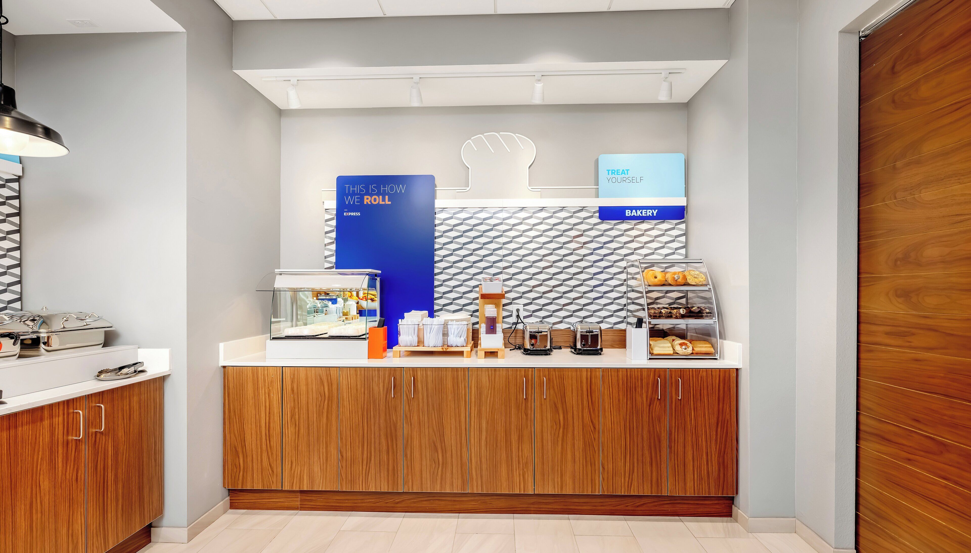 Eine Bäckereitheke mit einer Verkaufsvitrine, einer Kaffeemaschine und einem Schild mit der Aufschrift 'TREAT YOURSELF'.