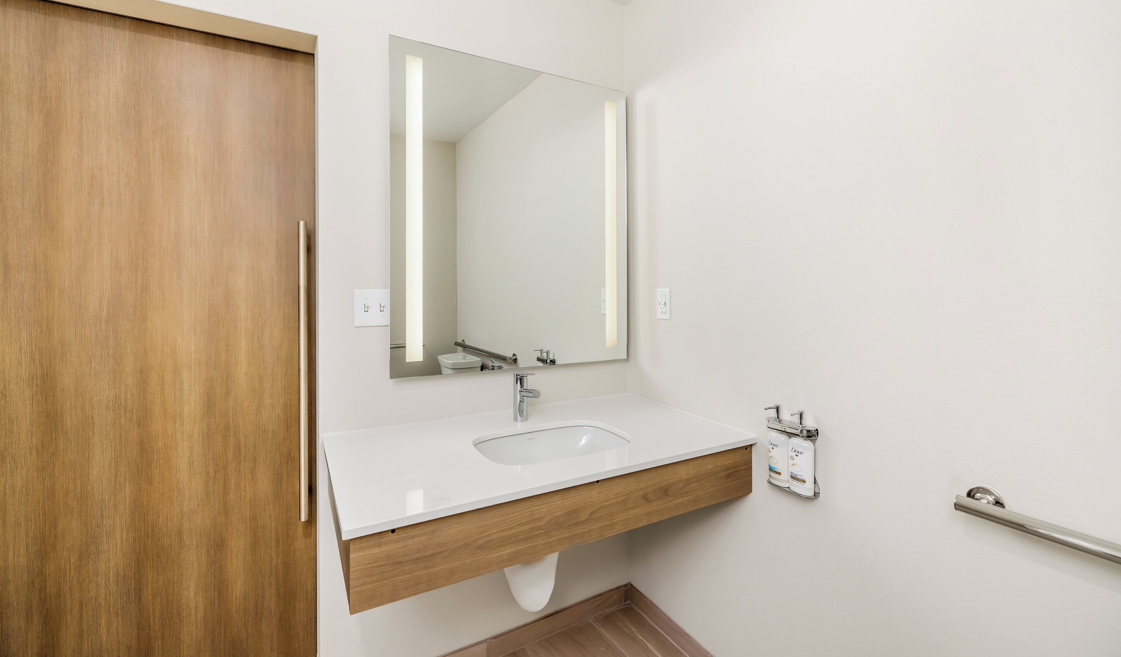 A bathroom with a white sink, wooden vanity, a mirror, and a handrail.