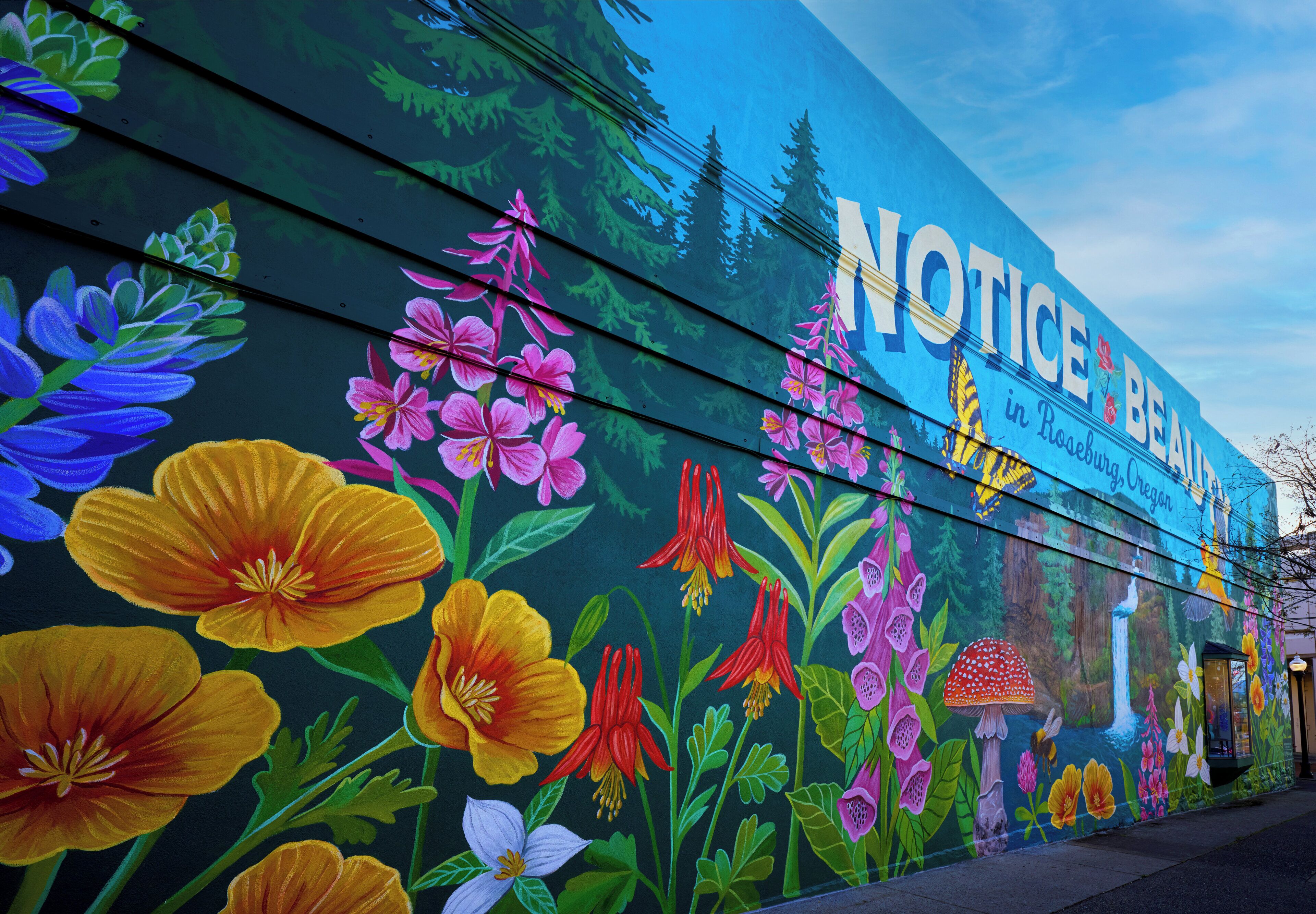 A mural with vibrant flowers and the text 'NOTICE BE AWAITS' on a building.