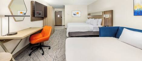 A hotel room with a desk, two beds, a TV, and artwork on the walls.