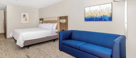 A hotel room with a bed, a blue sofa, a painting, and a lamp.