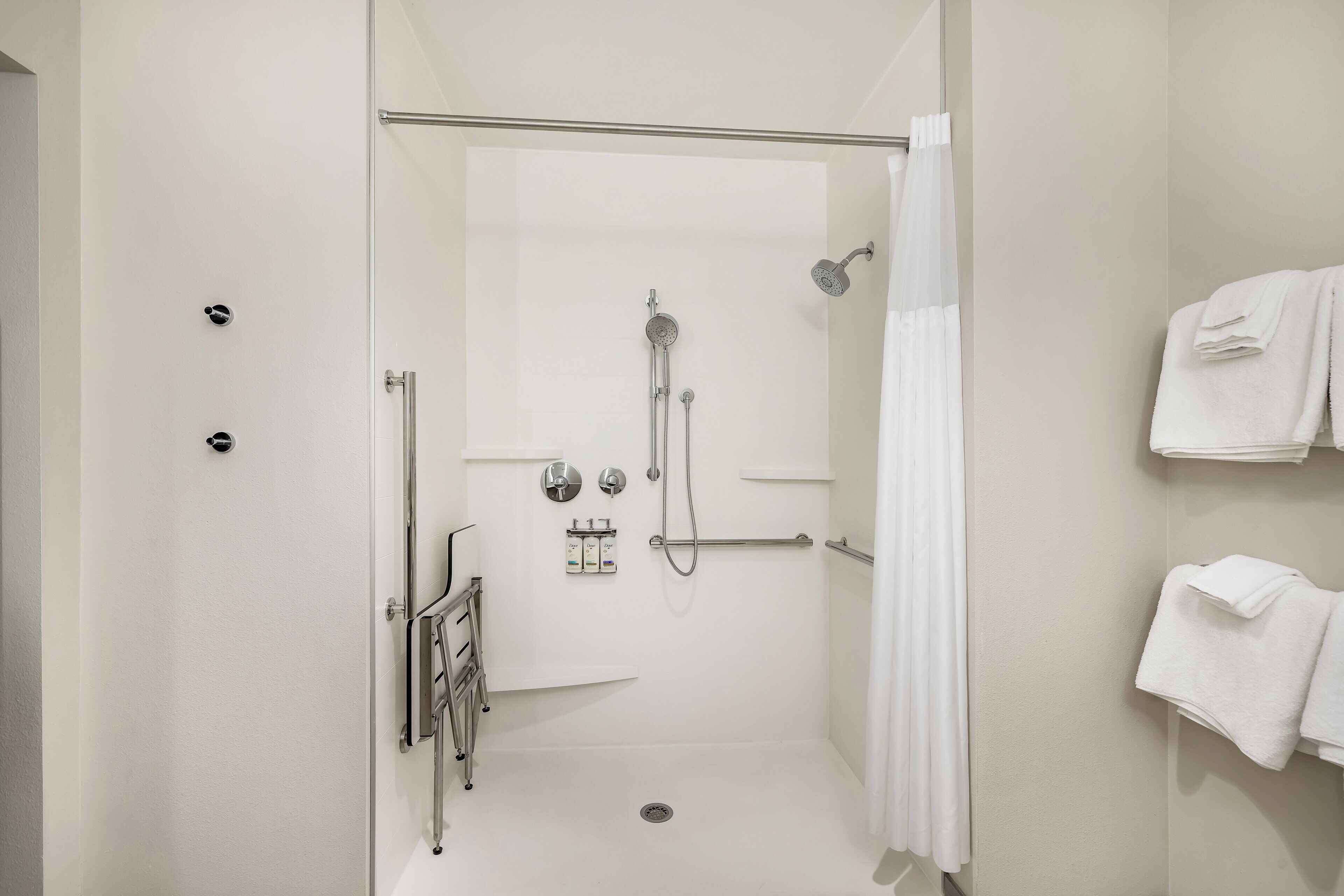 Ducha moderna con puerta de vidrio, cabezal de ducha de mano, grifo empotrado en la pared y toallero con toallas dobladas.
