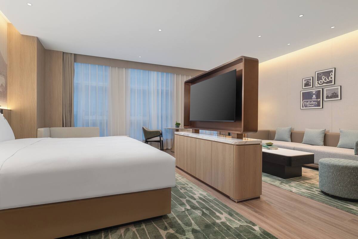 A modern hotel room with a large bed, a sofa, a TV, and a small table.