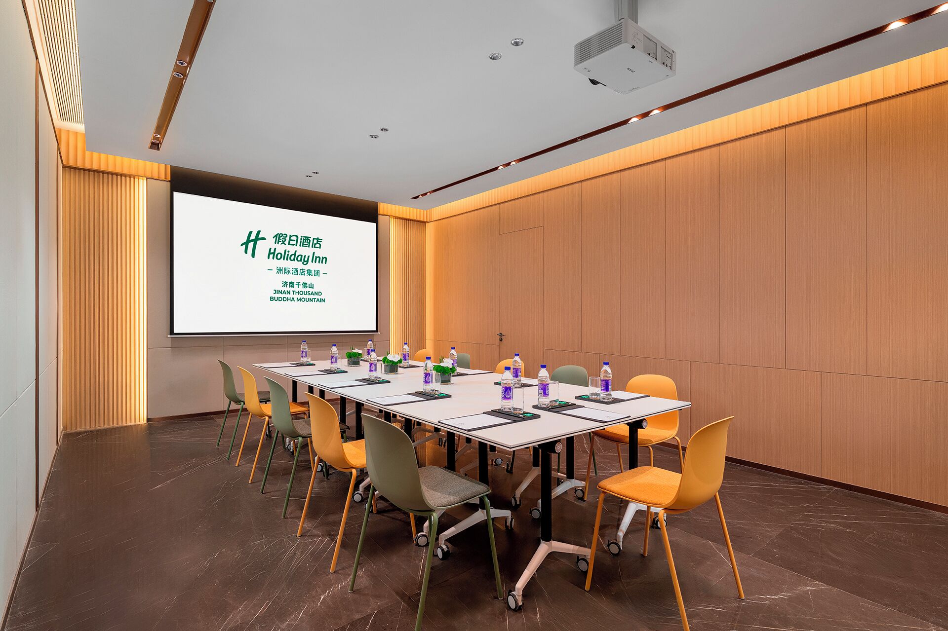 A conference room with a large screen displaying text, a long table with chairs, and a projector.