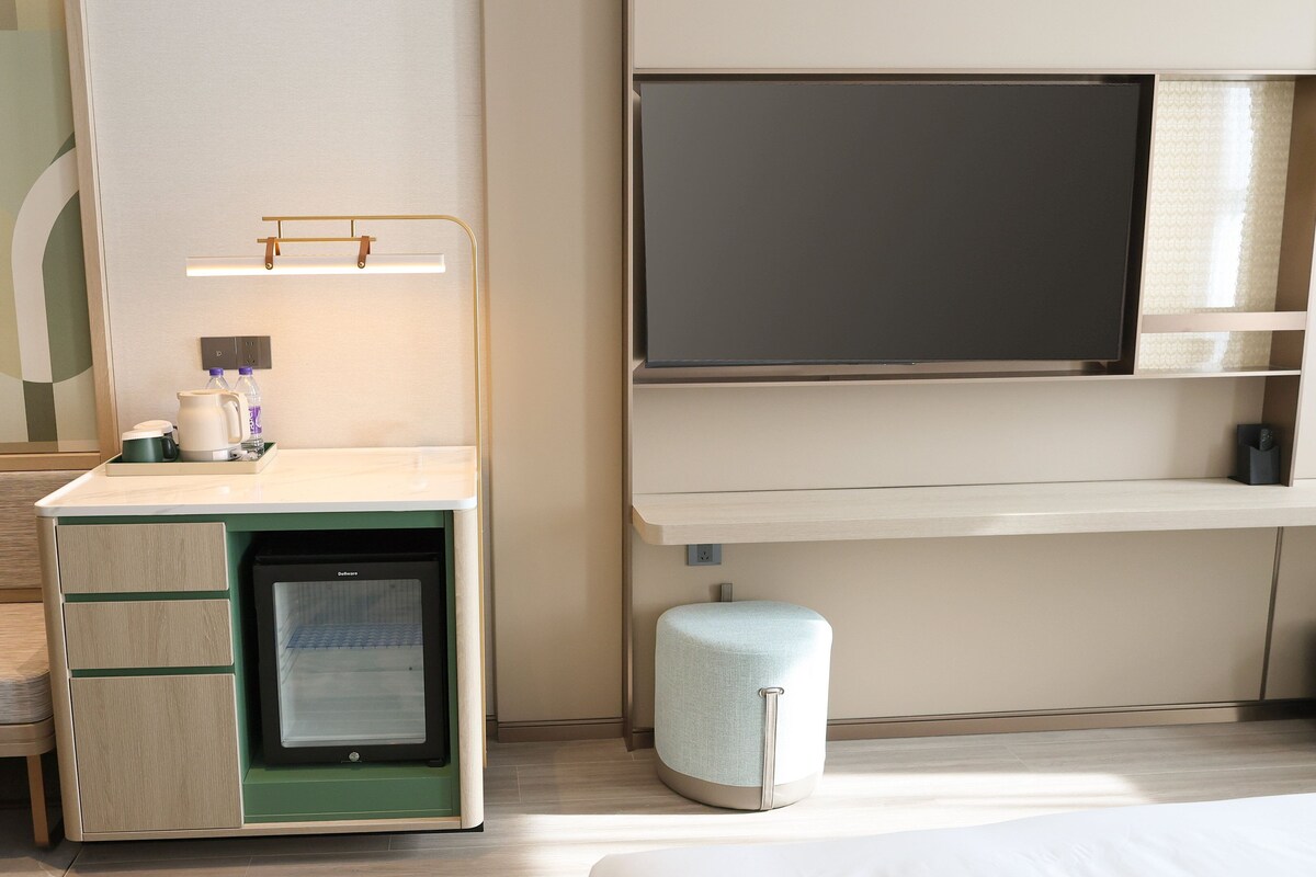 A hotel room with a desk, a small refrigerator, a television, and a seating area.