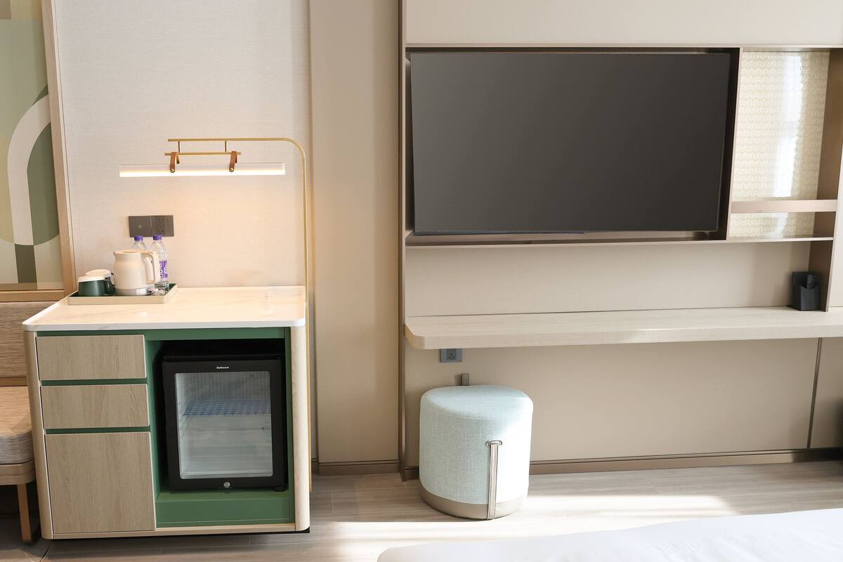 A hotel room with a desk, a small refrigerator, a television, and a seating area.