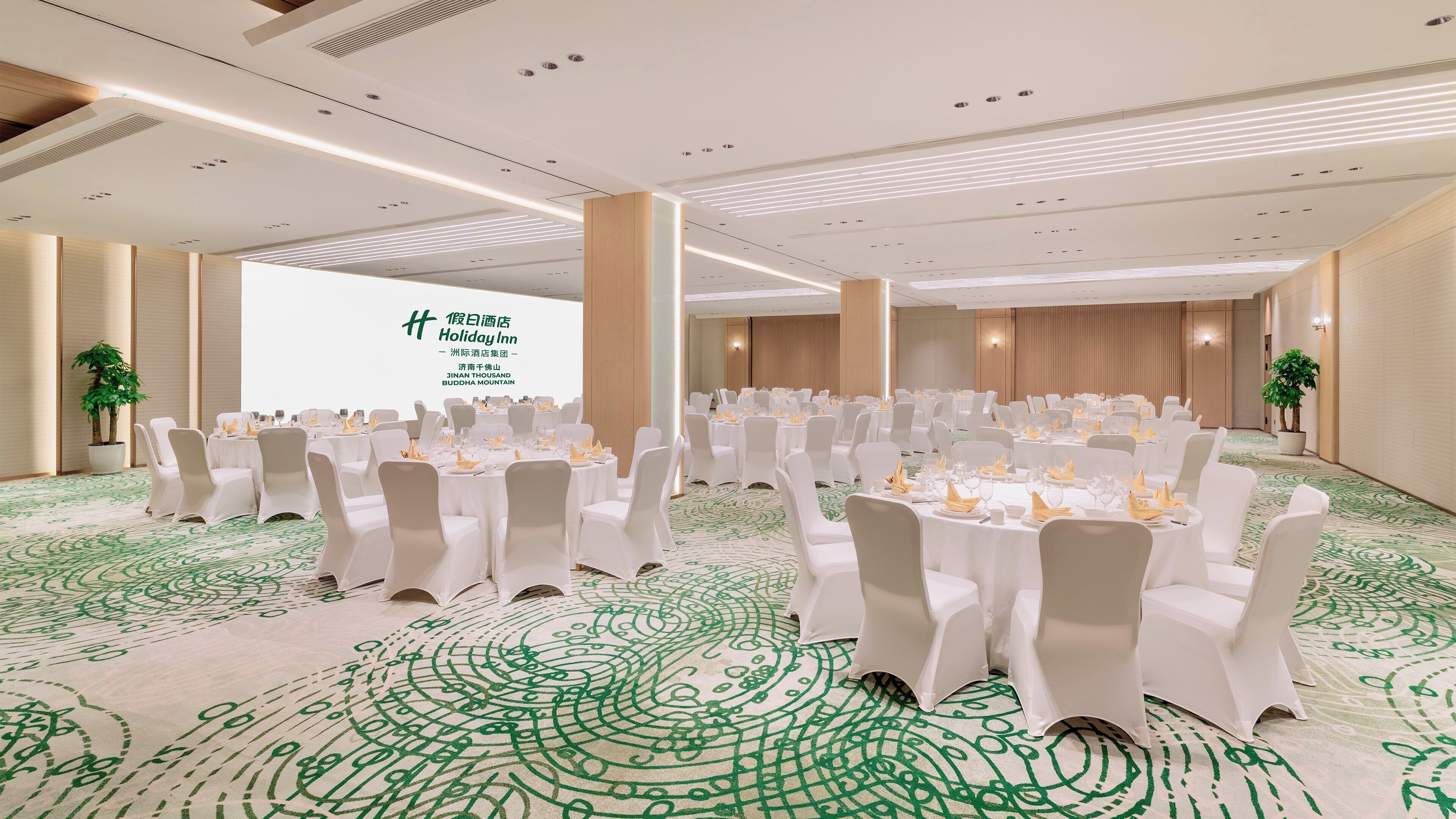 A conference room with round tables, white chairs, and a large screen displaying text.