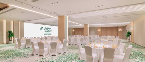 A conference room with round tables, white chairs, and a large screen displaying text.
