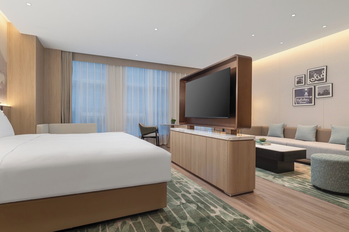 A modern hotel room with a large bed, a sofa, a TV, and a small table.