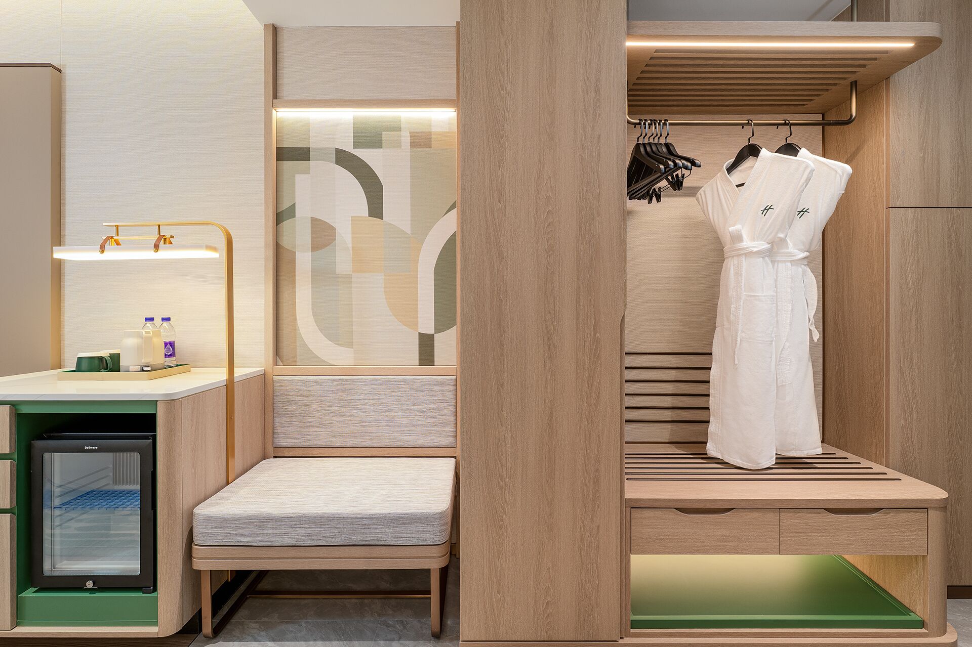 Una habitación de hotel compacta con kitchenette, zona de estar y vestidor con ropa colgada.