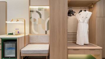 Una habitación de hotel compacta con kitchenette, zona de estar y vestidor con ropa colgada.