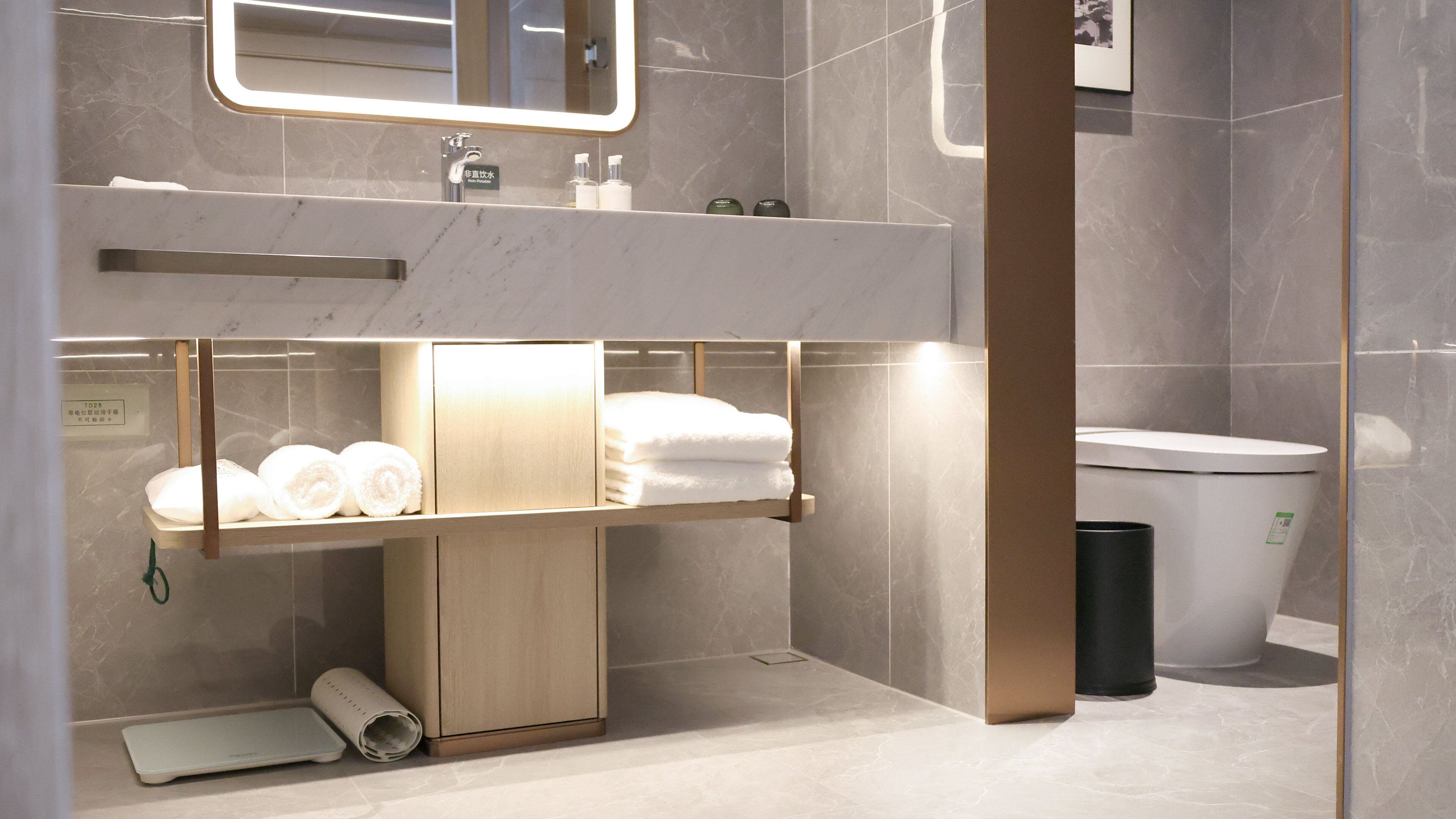 A modern bathroom with a marble vanity, a toilet, and a shelf with towels.