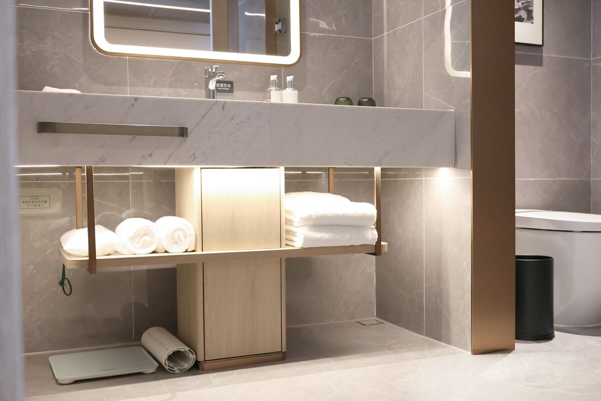 A modern bathroom with a marble vanity, a toilet, and a shelf with towels.