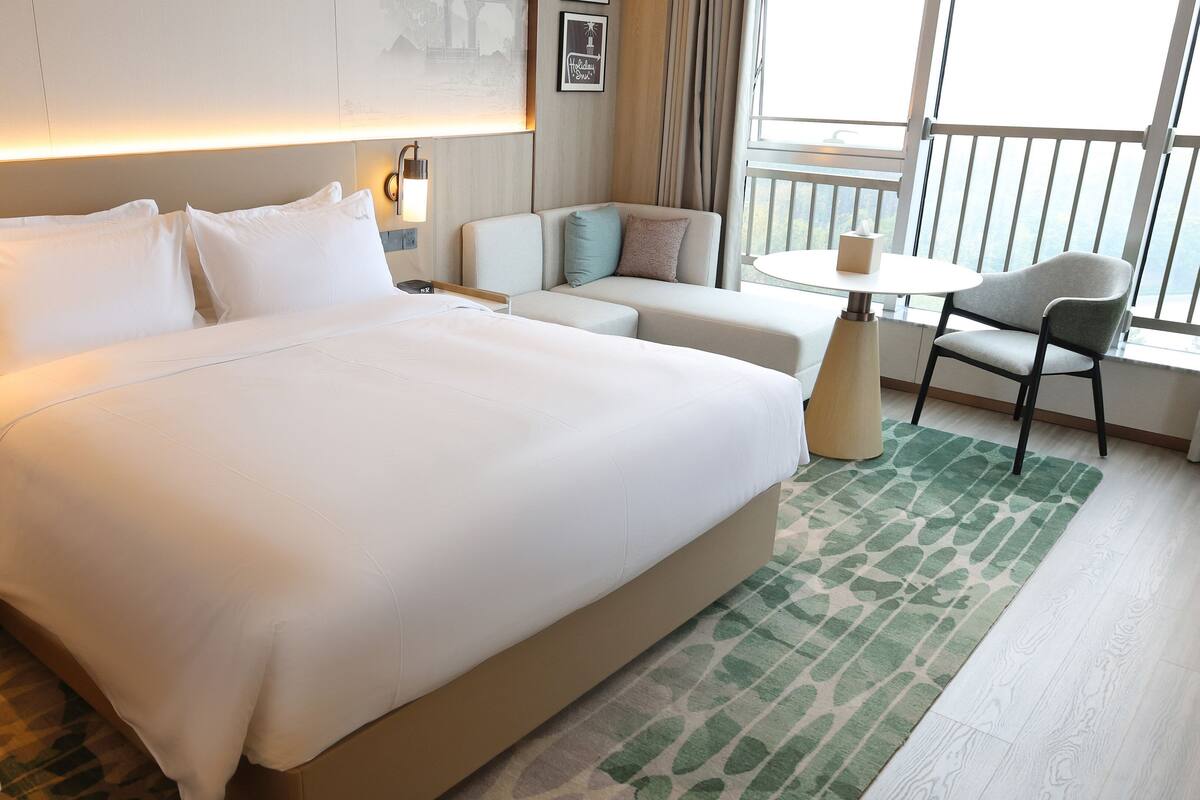 A hotel room with a large bed, a sofa, a small table, and a chair.