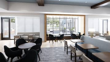 A modern hotel lobby with seating areas, tables, and large windows offering views of the outdoors.