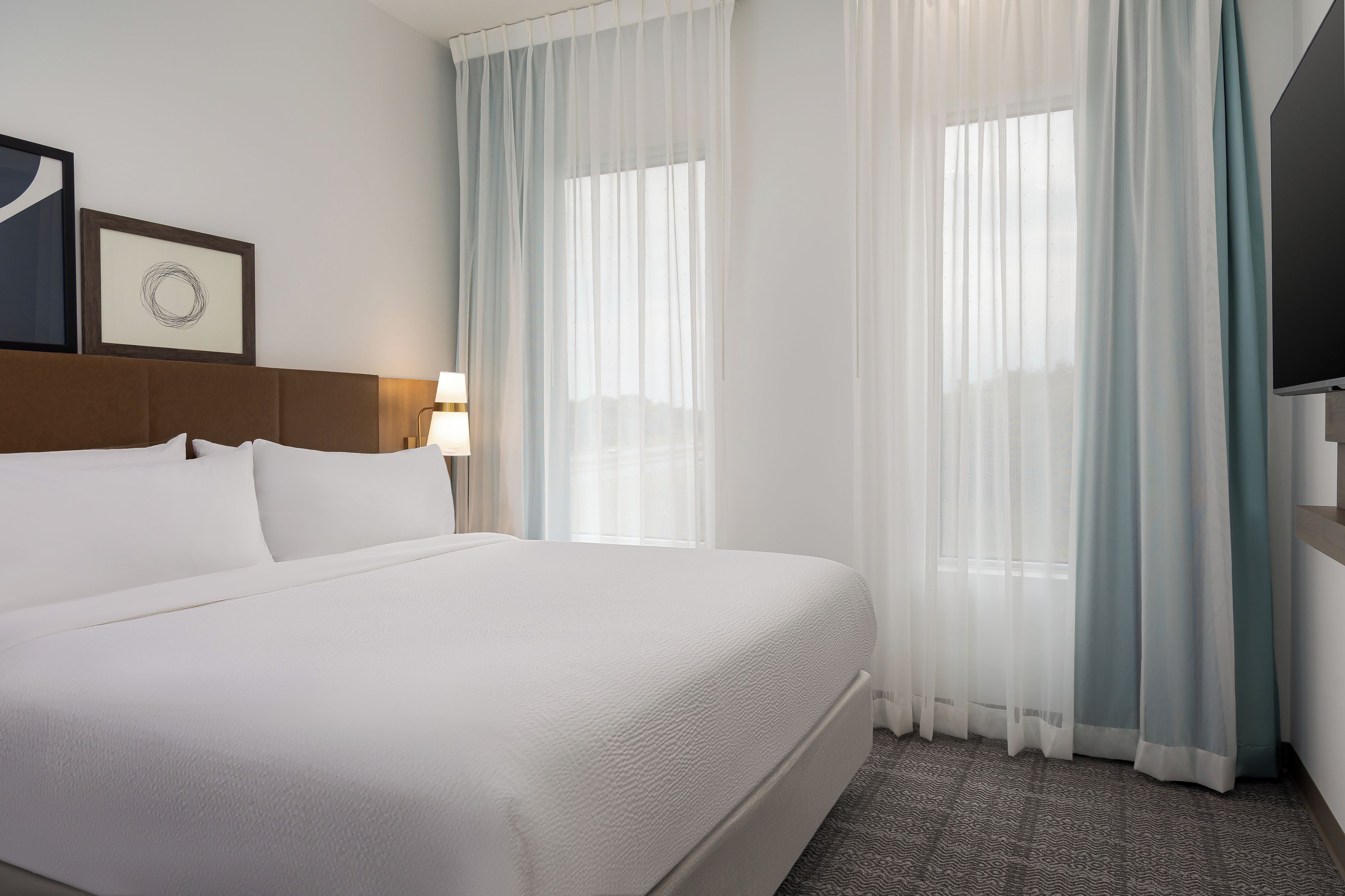 Une chambre d’hôtel avec un grand lit, une tête de lit, une lampe de chevet, un téléviseur à écran plat et des rideaux en voile.