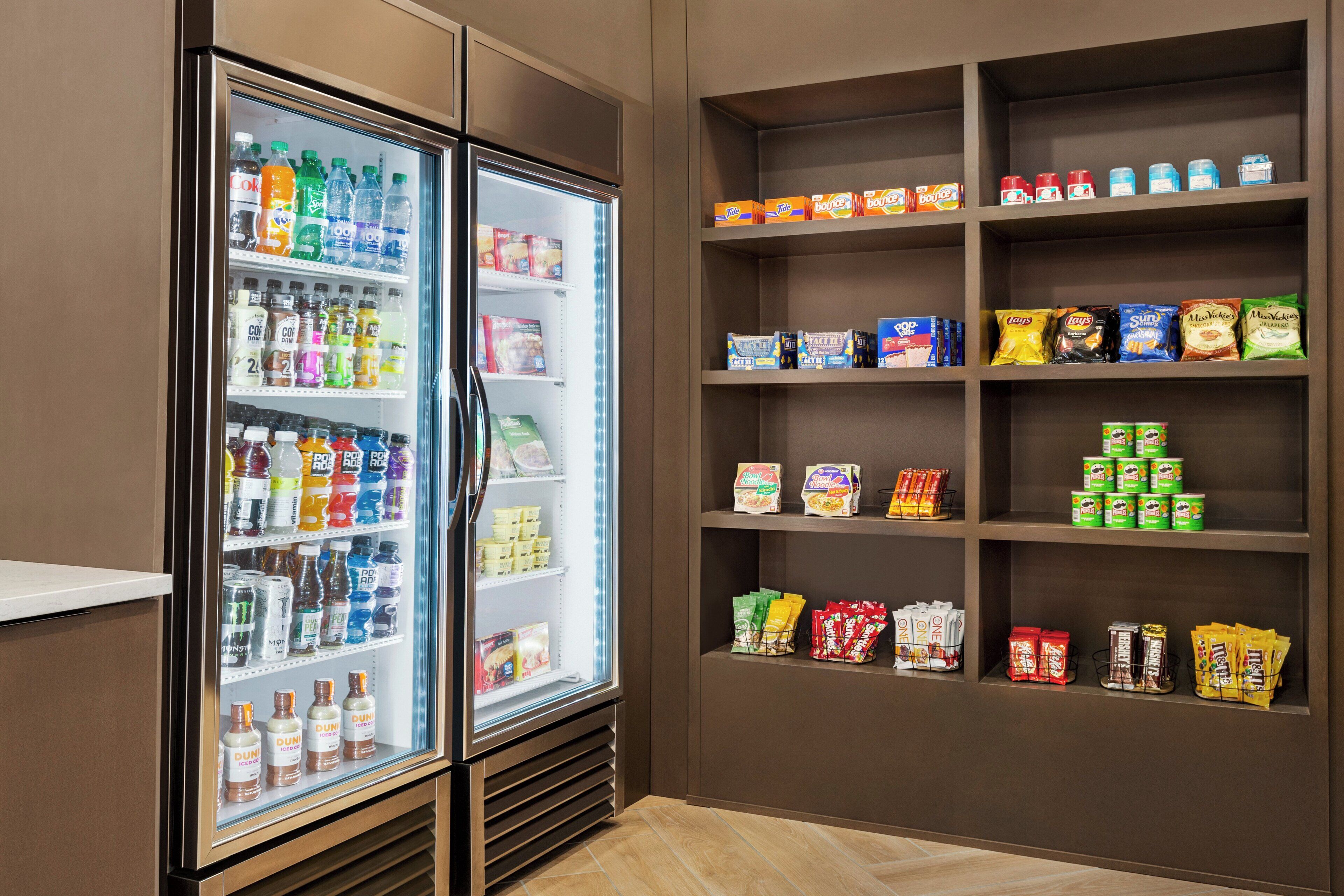 A refrigerated display case with various beverages and a shelf stocked with snacks and packaged foods.