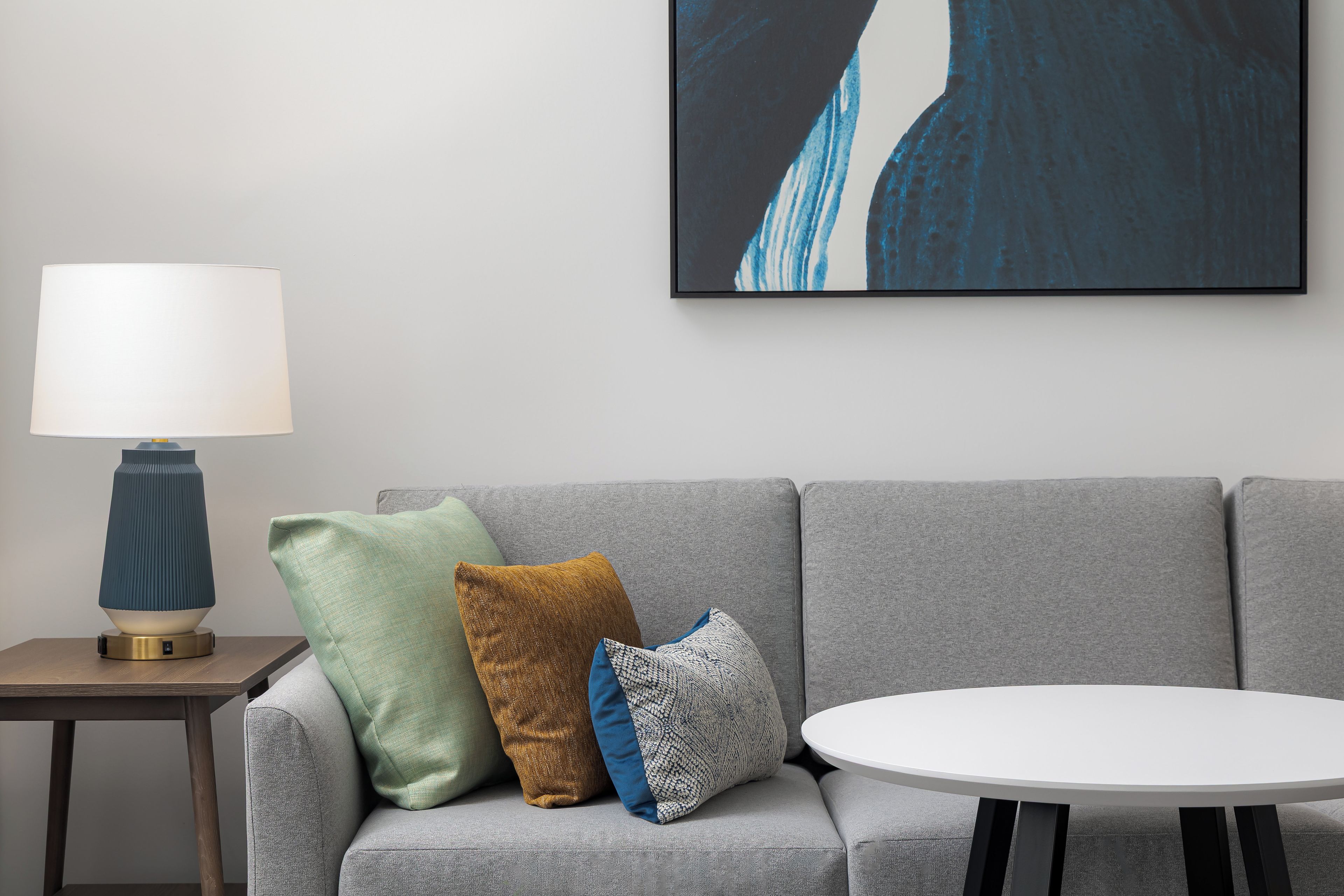 A modern living room with a grey sofa, a round white table, and a lamp on a side table.