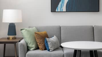 A modern living room with a grey sofa, a round white table, and a lamp on a side table.