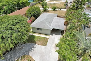 A residential house with a sloped roof, surrounded by lush greenery and a paved driveway.