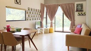 A modern living room with a dining area, large windows with curtains, a flat-screen TV, and a wall-mounted clock. - Electus Home at Midhills Genting - Free WiFi & Parking (Genting Highlands)