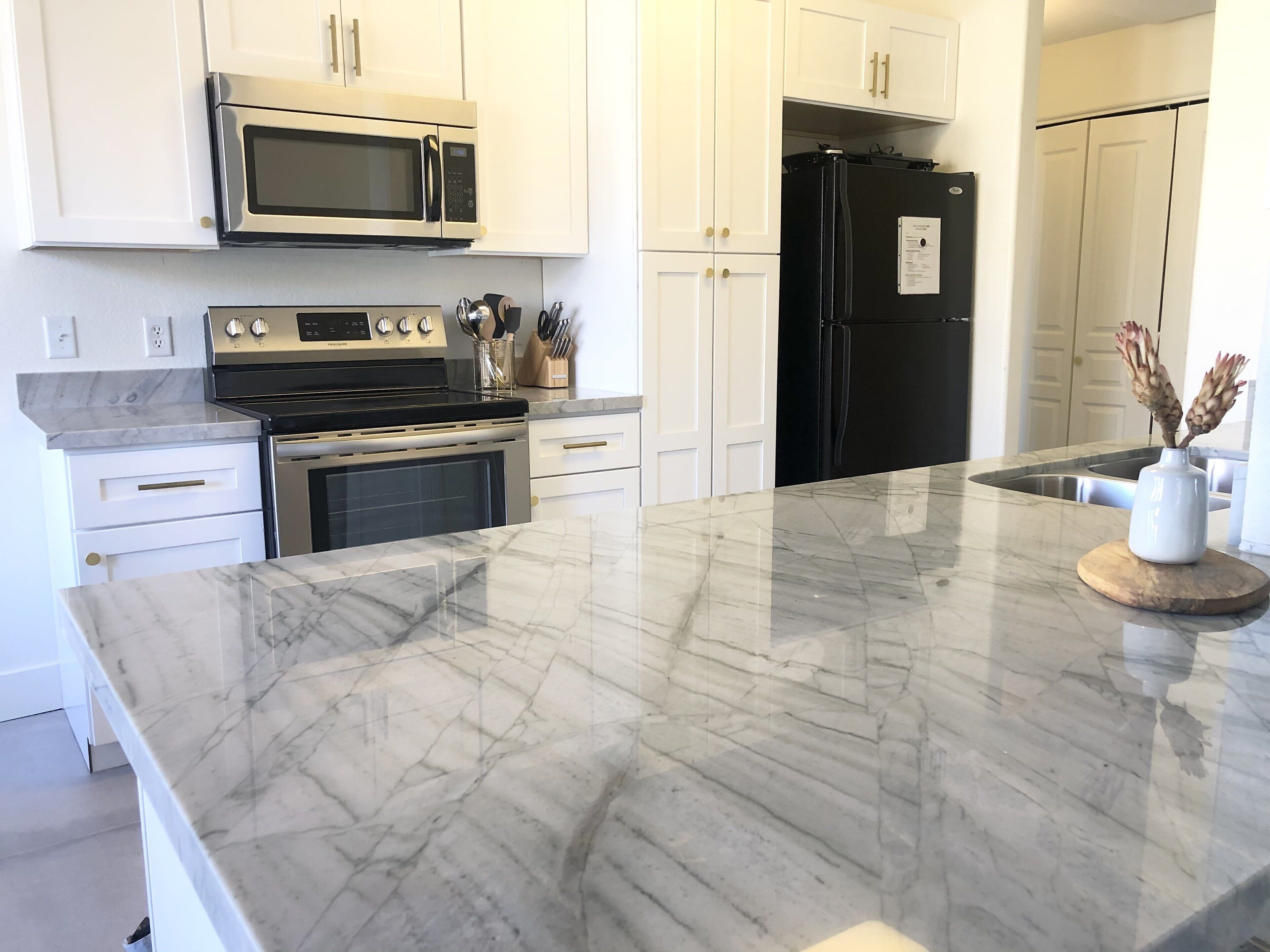 A modern kitchen with white cabinets, stainless steel appliances, and a marble countertop.