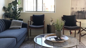 A living room with a sofa, two chairs, a coffee table, a large window, a plant, and a painting on the wall. - Gilbert/Mesa 2 Bedroom Condo, right next to heated pool! (Mesa)