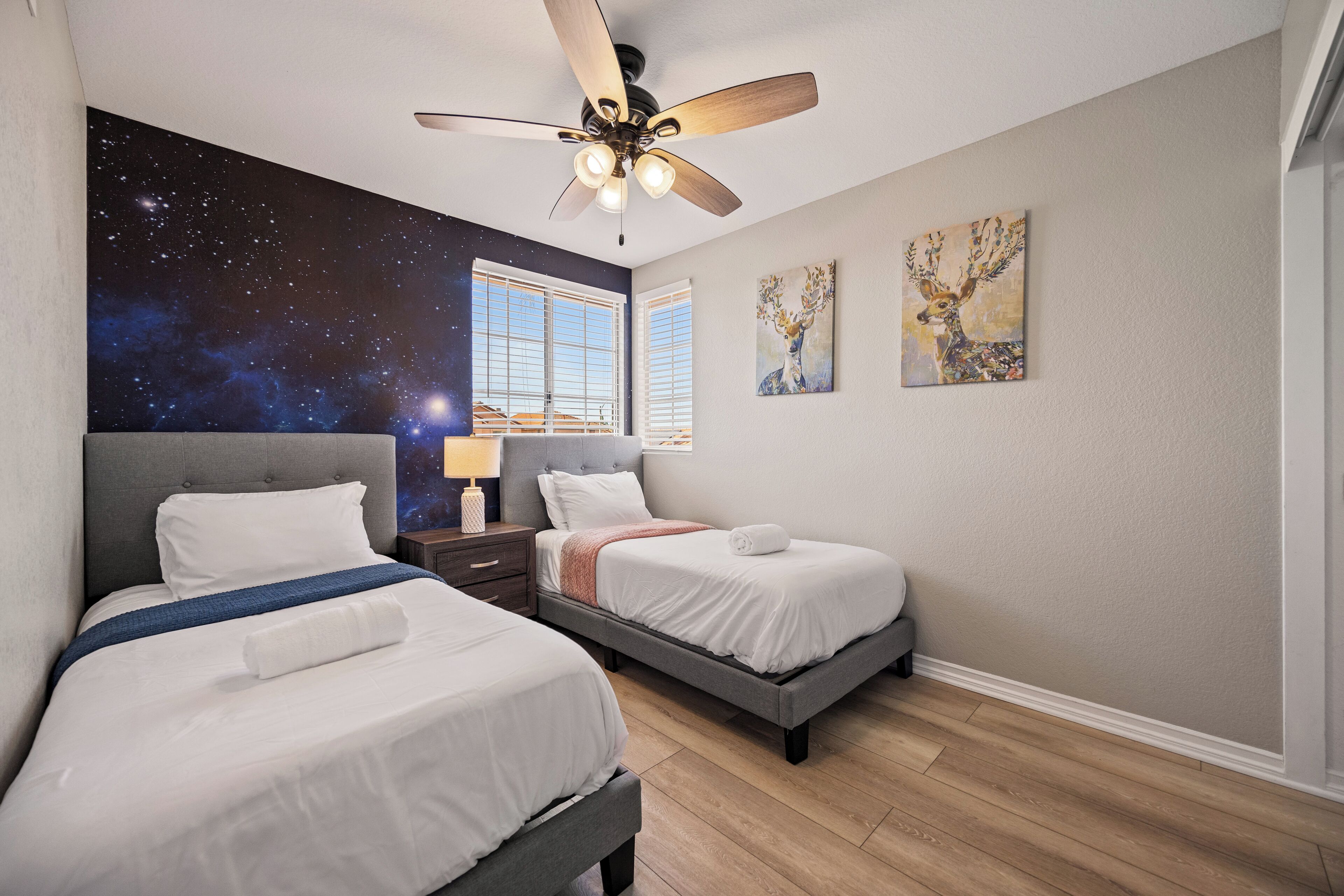 Un dormitorio con dos camas, ventilador de techo, mural de estrellas en la pared y obras de arte.