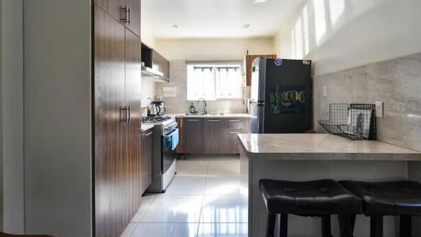 A modern kitchen with wooden cabinets, a stainless steel refrigerator, and a bar area with stools. - For 6, NO stairs, beach, Costco, well located! (Mérida)