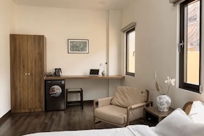 Une chambre d’hôtel compacte comprenant un lit, un bureau avec un ordinateur portable, une chaise, une petite table, une armoire et une fenêtre donnant sur un paysage agréable.