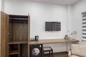 A room with a wooden wardrobe, a desk with a chair, a television on the wall, and a window with blinds. - Signy House City Center (Ho Chi Minh City)