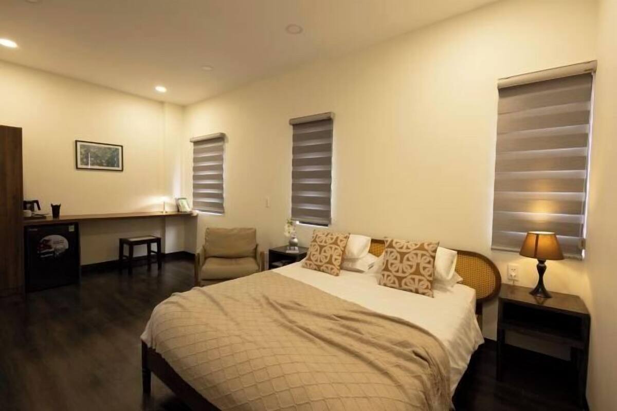 A bedroom with a bed, bedside tables, a desk, a chair, and a window with blinds.